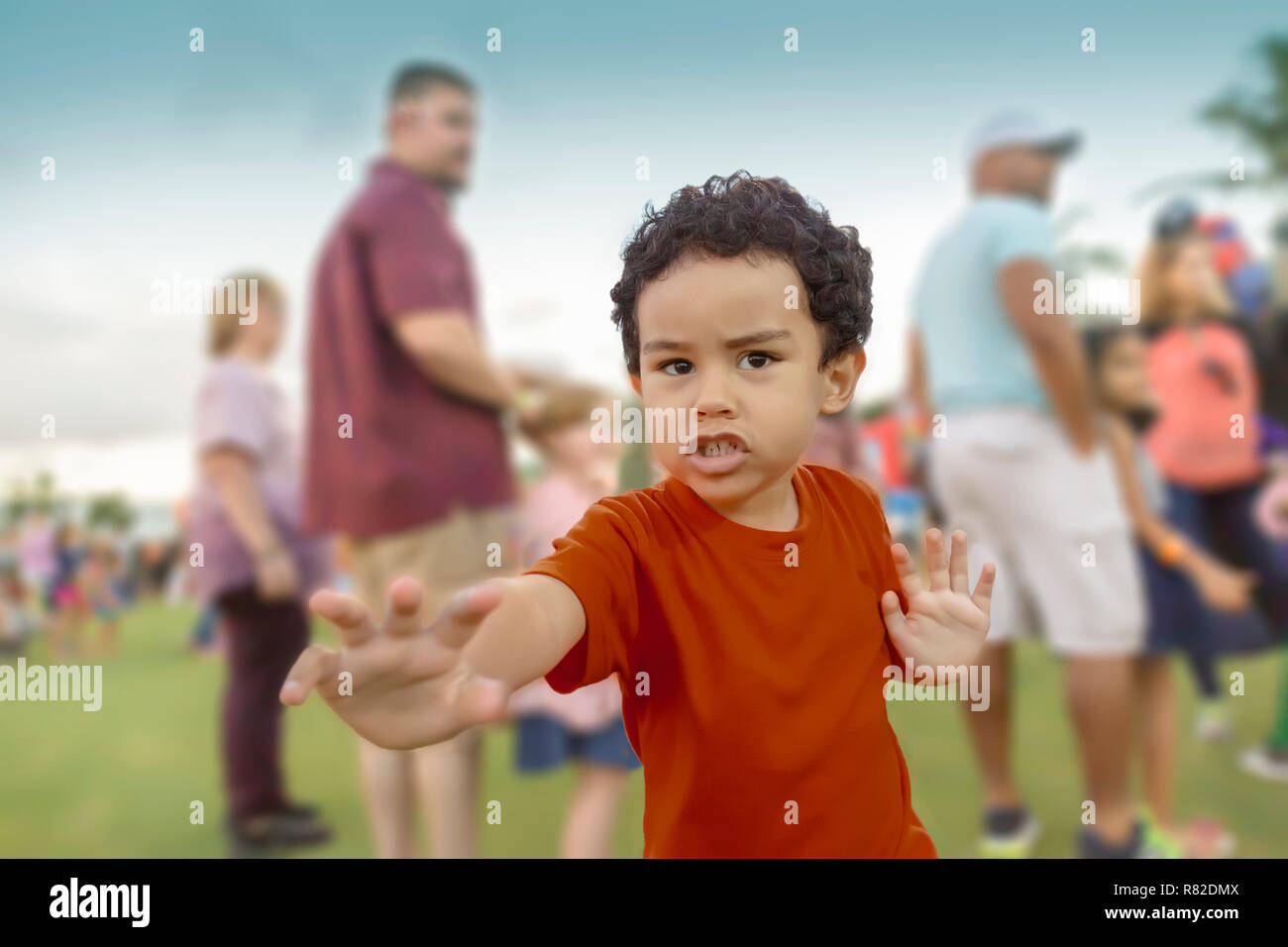 A small ethnic boy in a red shirt likes to show off while waiting in line. As parents wait with their kids for the next ride to open. Stock Photo