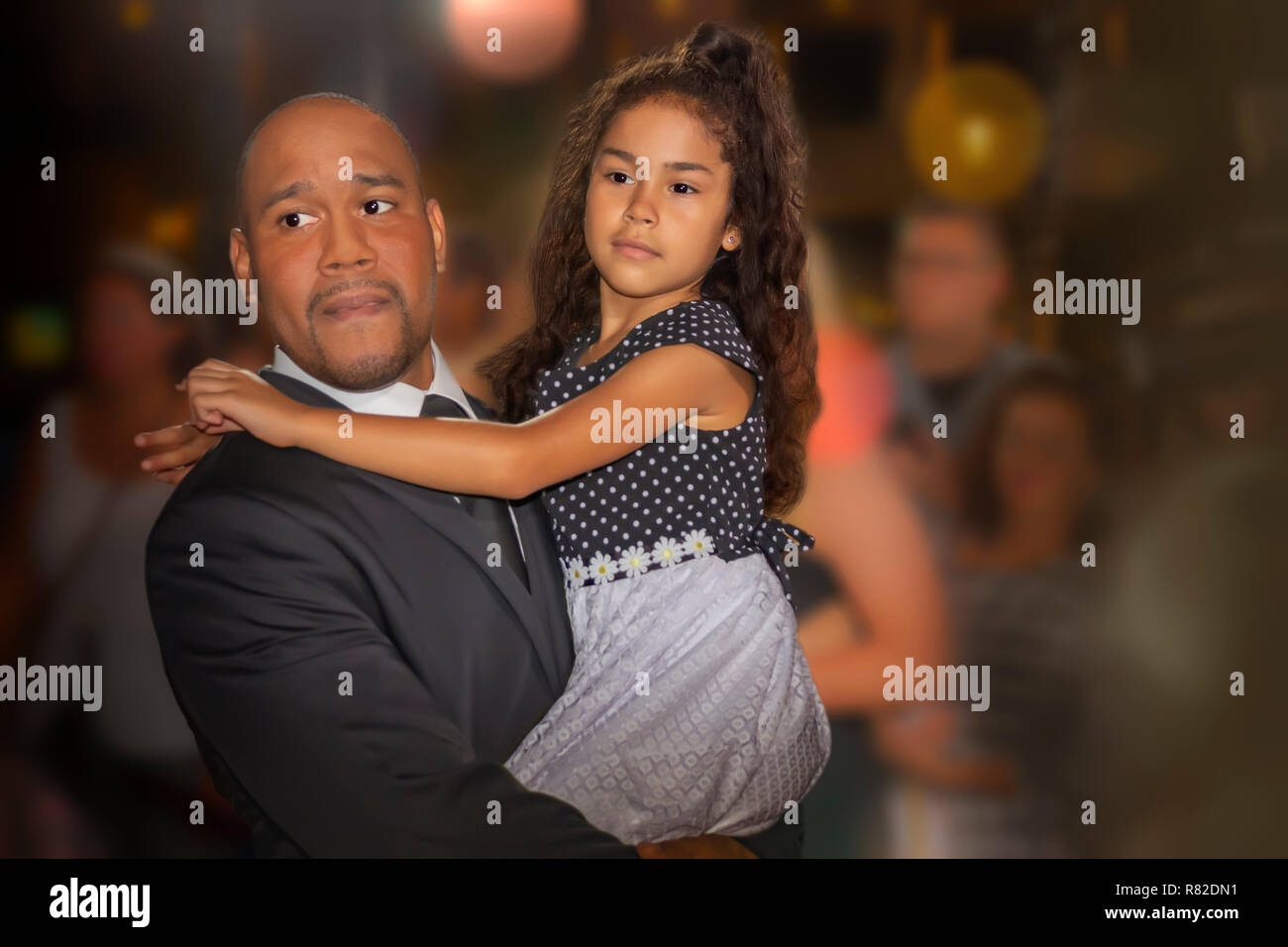 Father with a young daughter in his armsFather is wearing a black suit with a black tie and child has on a formal long neutral color dress. Stock Photo