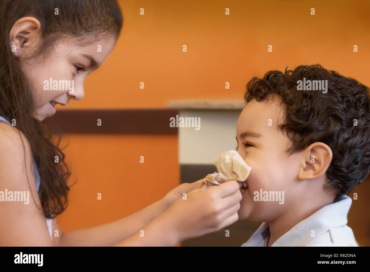 Big sister helps little brother blow his nose. Older sister focused on wiping younger brothers nose as he laughs. Stock Photo