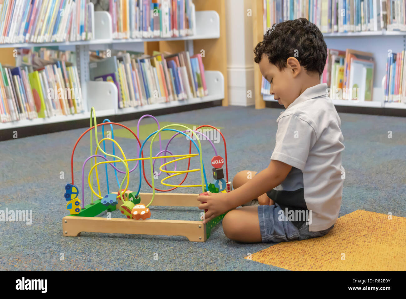 Profile of a little boy at play on the carpeted library floor.  Alone and happy in the corner play area at daycare. Stock Photo