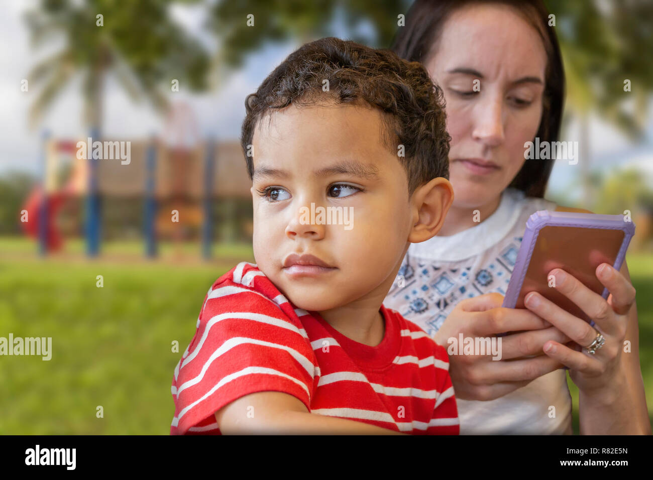 Mommy and her boy relax at the playground. A mother spends quality time with her son at the park when she receives a text message. Stock Photo