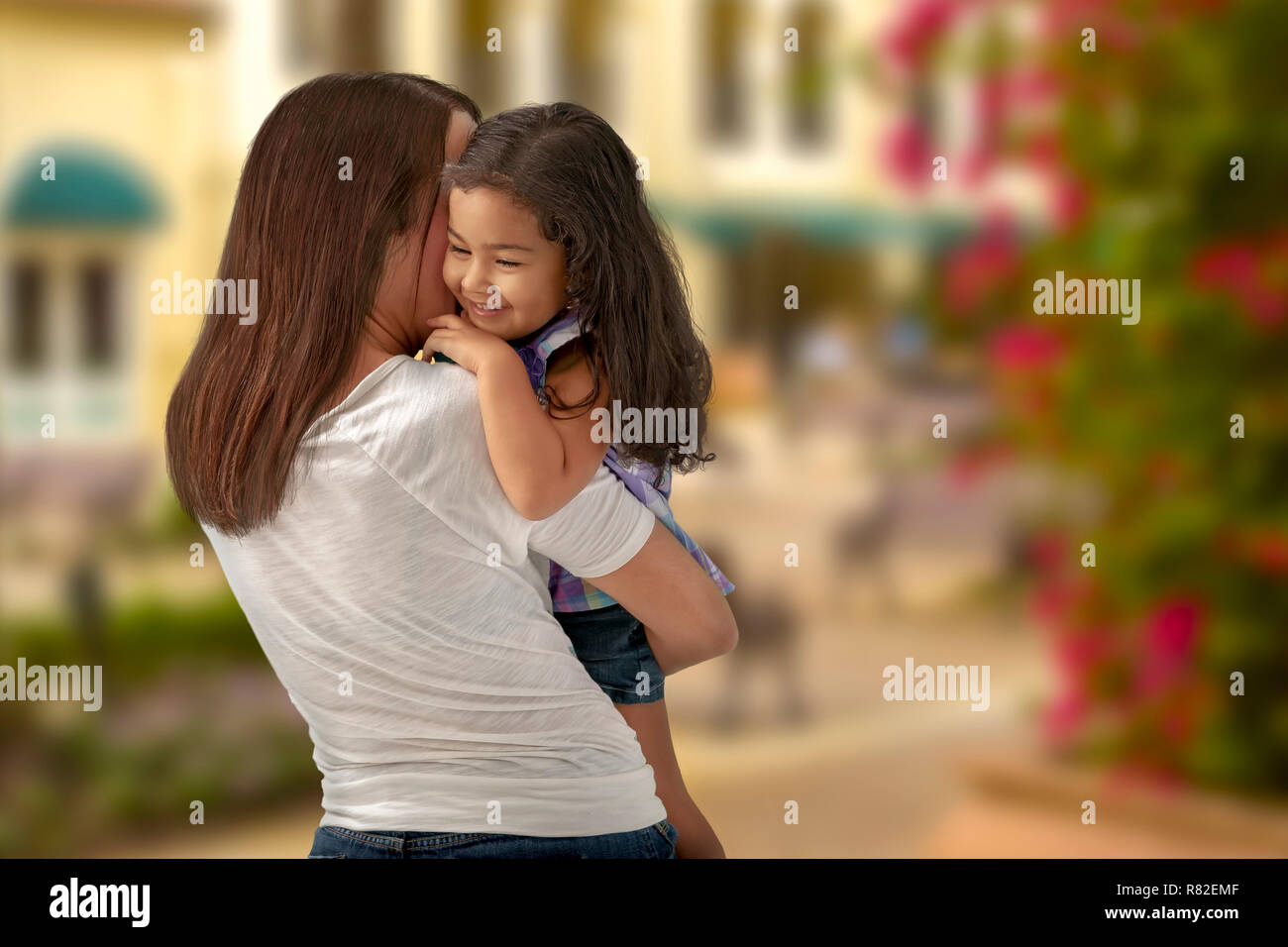 A smiling young daughter in her mother's arms clings close as they walk away. A warm sunny soft background completes a precious moment. Stock Photo