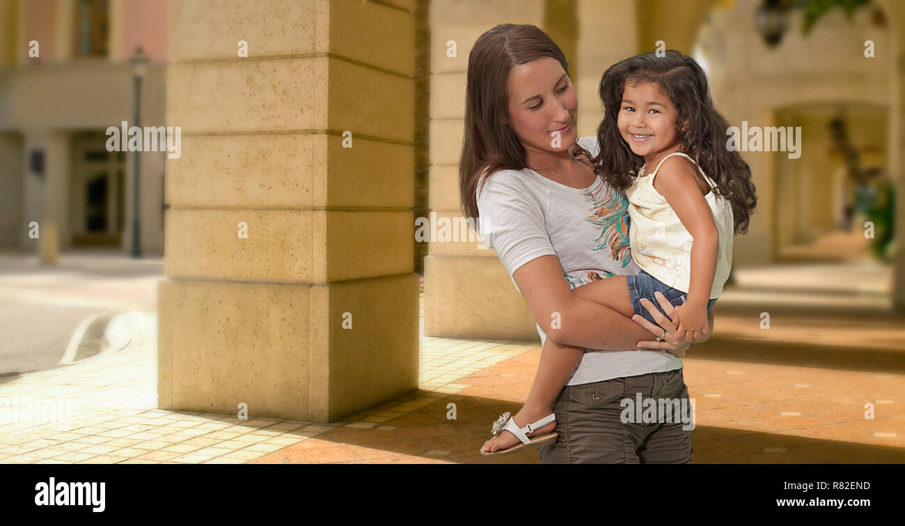 Outside the shopping center a mother bonds with her happy young daughter holding her close in her arms as she enjoys the child's smile. Stock Photo