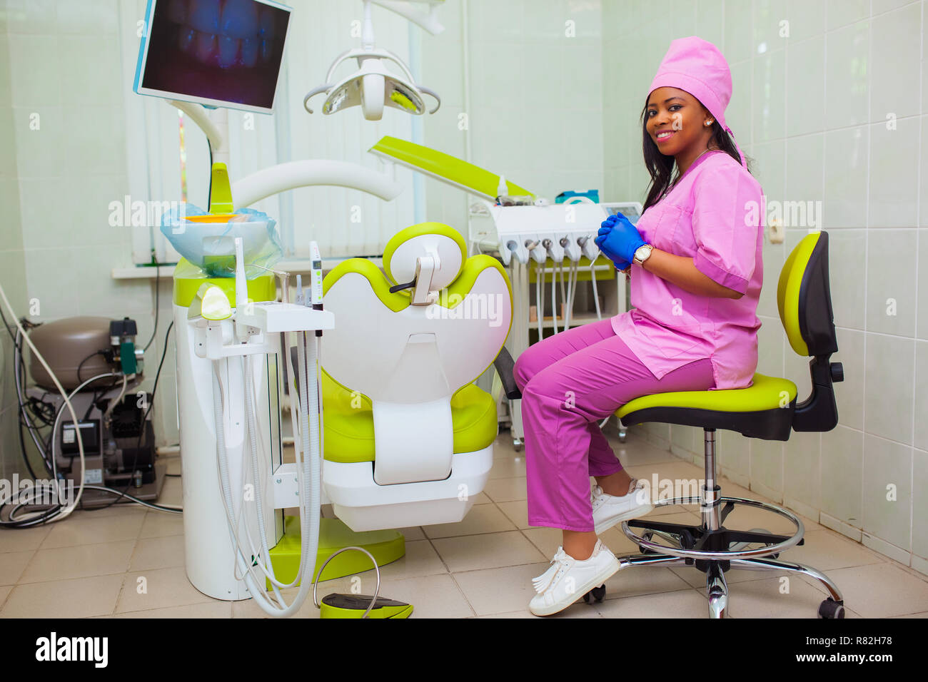 Young smiling black ethnic AfroAmerican female dentist assistant standing in dental office by