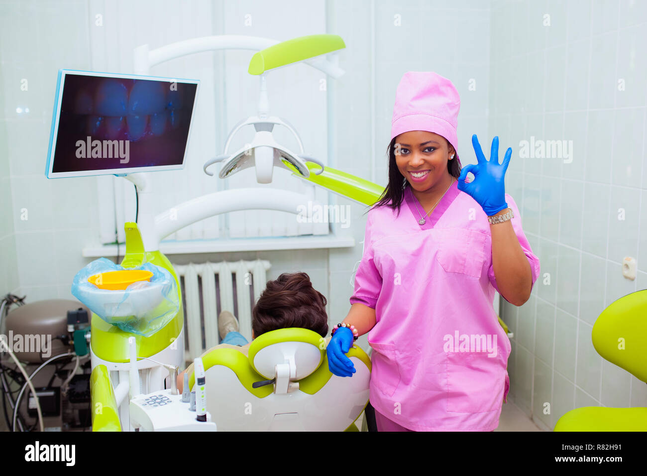 Young smiling black ethnic AfroAmerican female dentist assistant standing in dental office by