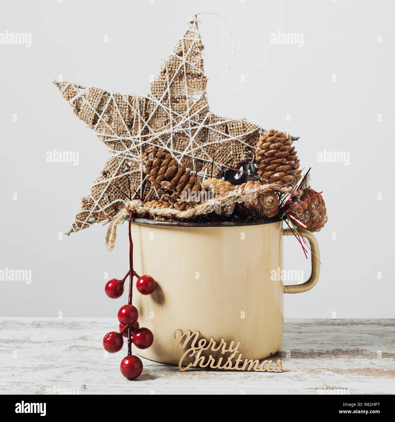 closeup of some different cozy christmas ornaments in a rustic brown enamel pot and the text merry christmas in three dimension, on a rustic wooden su Stock Photo