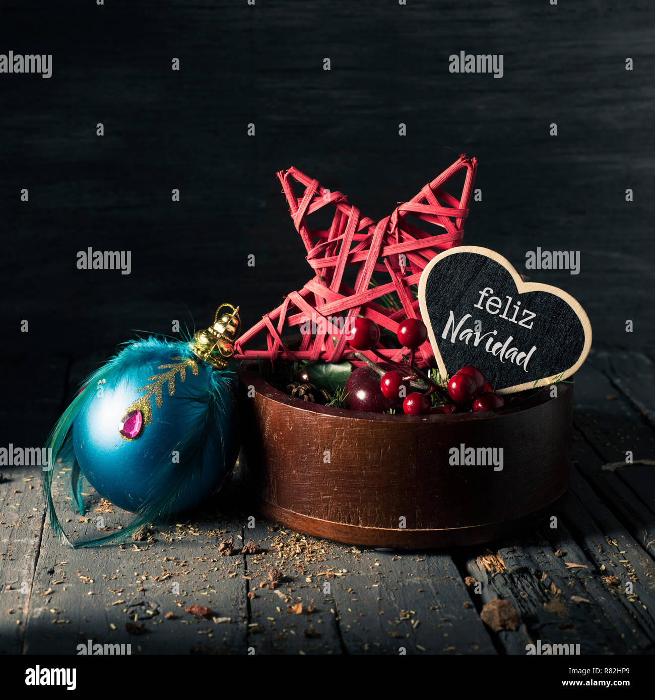 some cozy christmas ornaments in a wooden tray and a heart-shaped black signboard with the text feliz navidad, merry christmas written in spanish Stock Photo