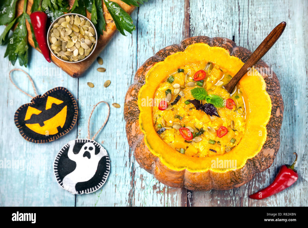 Soup with lentil in the carved pumpkin, ghost and laughing black lantern toys on the blue wooden background at Halloween party Stock Photo
