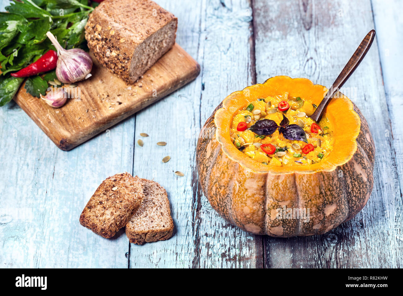 Soup with lentil decorated in the carved pumpkin with bread pieces on the blue wooden background at autumn holidays Stock Photo