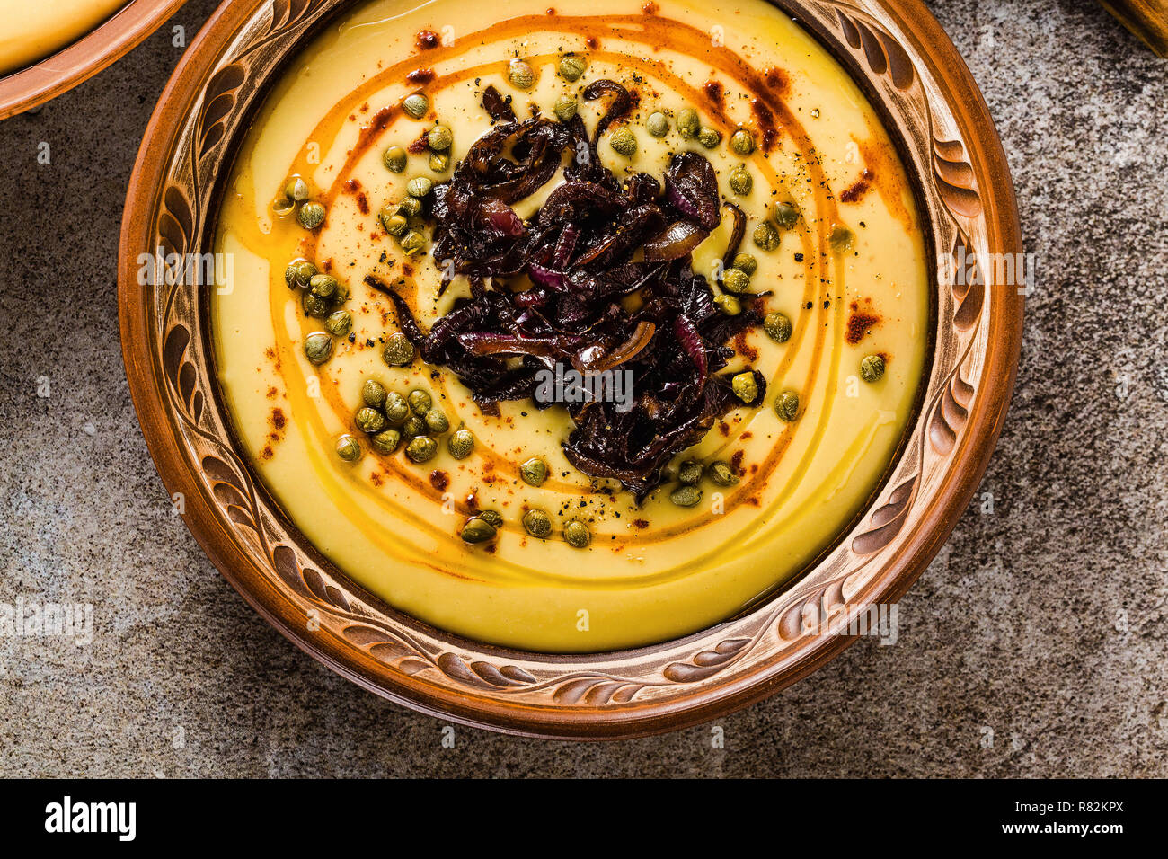 Authentic Greek Fava recipe, Middle Eastern yellow lentil soup with caramelized onions, paprika and capers. vegan healthy food in clay pots on the sto Stock Photo