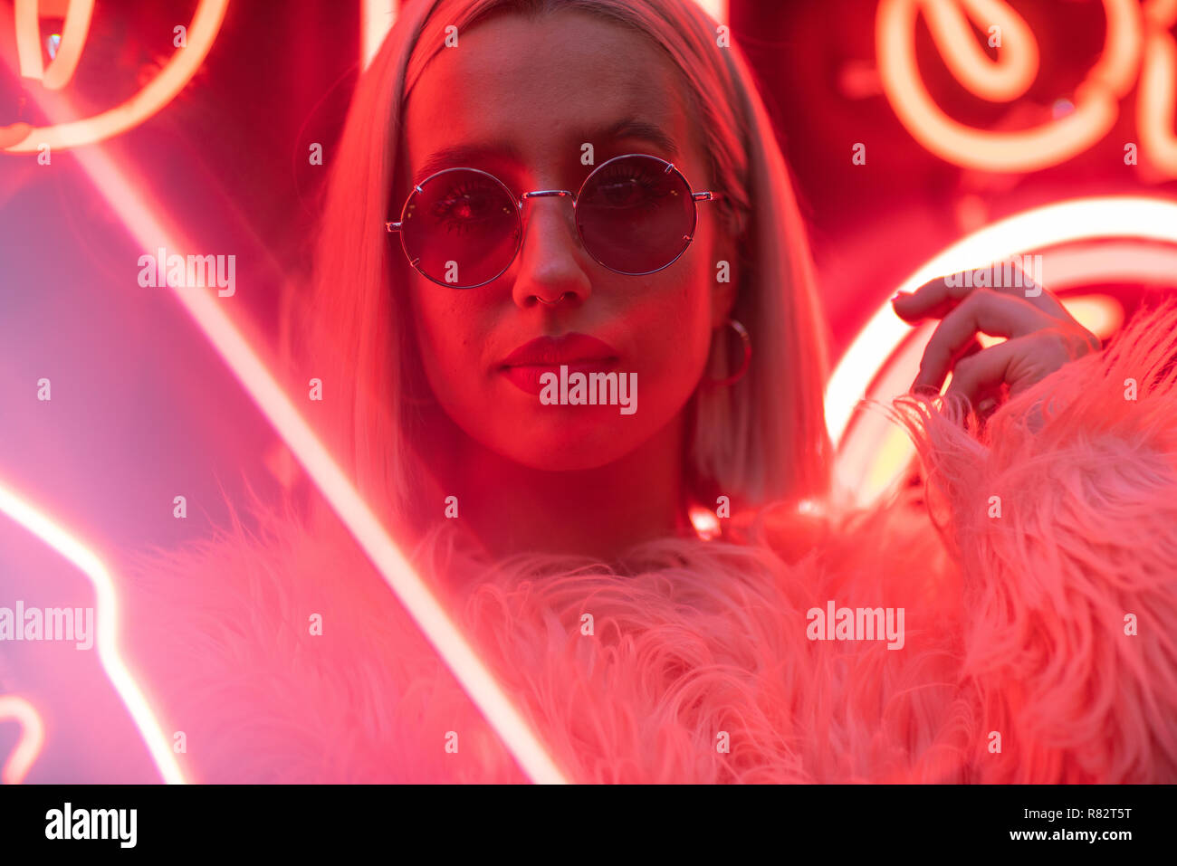 Cinematic portrait of blond girl with furry pink coat on neon sign at ...