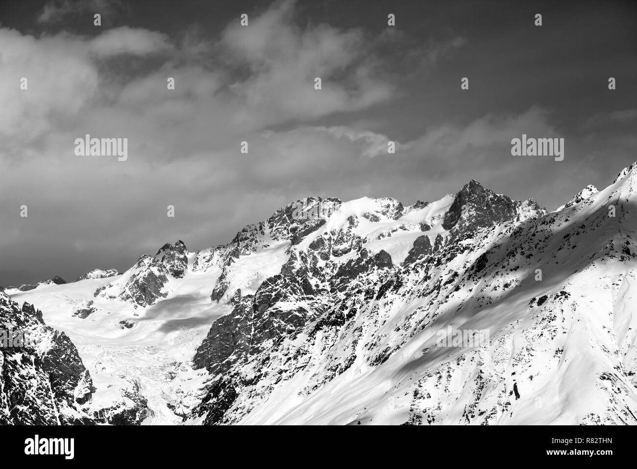 View on snowy mountains with glacier and cloudy sky in nice sunny day. Caucasus Mountains at winter. Svaneti region of Georgia. Black and white toned  Stock Photo