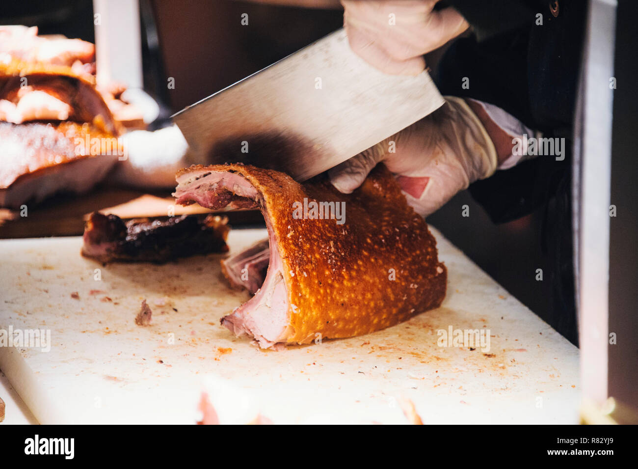 Close up view of hands chopping roast pig ribs with a large meat cleaver Stock Photo