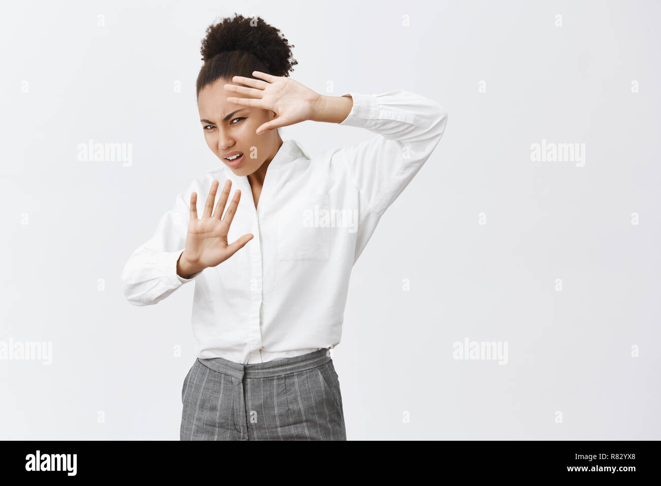 Wow, turn light off man. Disturbed and displeased african-american businesswoman in white shirt and pants, lifting hands to cover face from sparks of ligtning, frowning from healight on car Stock Photo