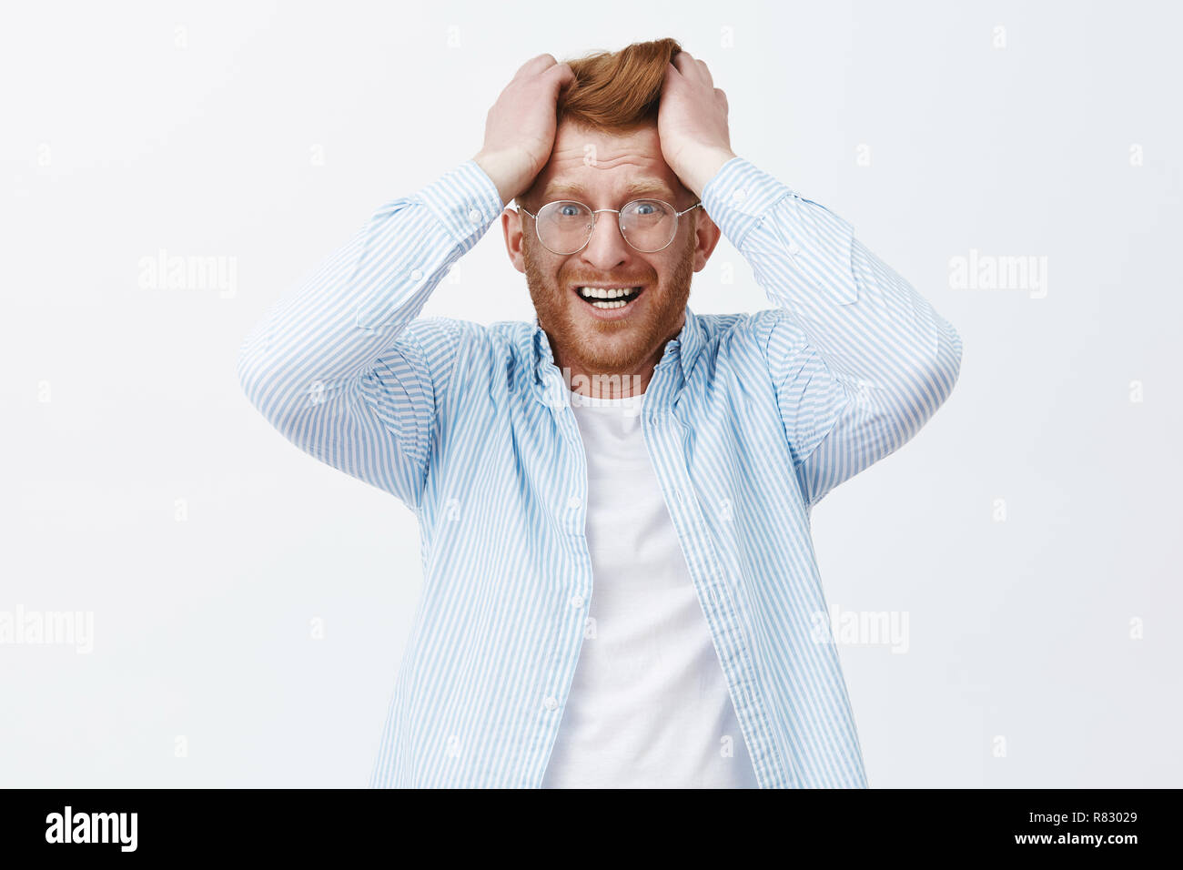 Studio shot of upset redhead man in despair and shook, feeling distressed losing company, pulling hair out of head, frowning and grimacing from painful feelings, standing over gray background Stock Photo