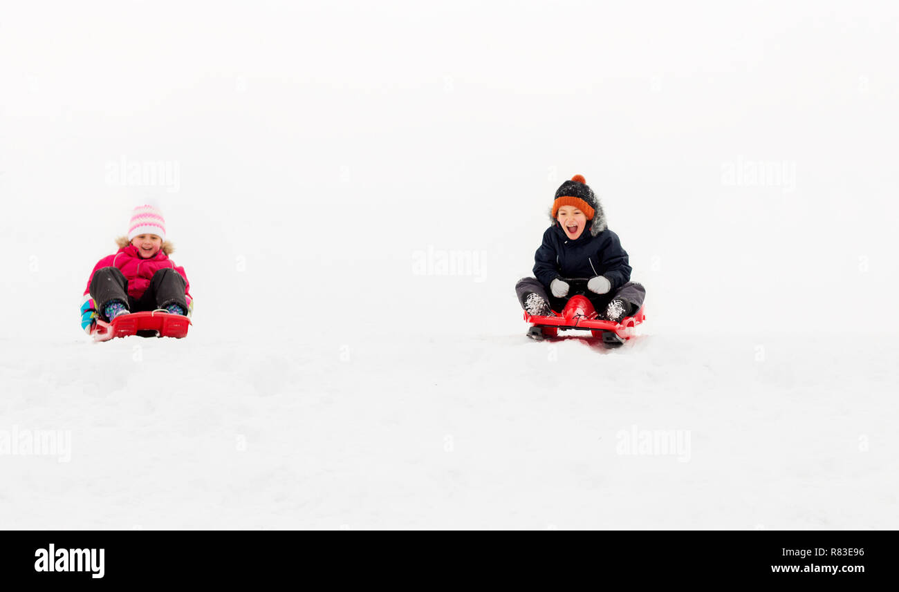 kids sliding on sleds down snow hill in winter Stock Photo