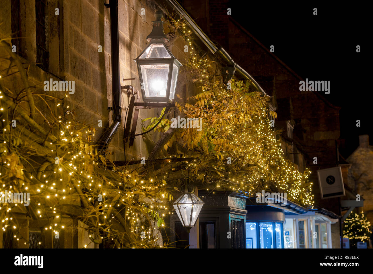 Street lamps and christmas fairy lights outside Broadway shops at night. Broadway, Cotswolds, Worcestershire, England Stock Photo