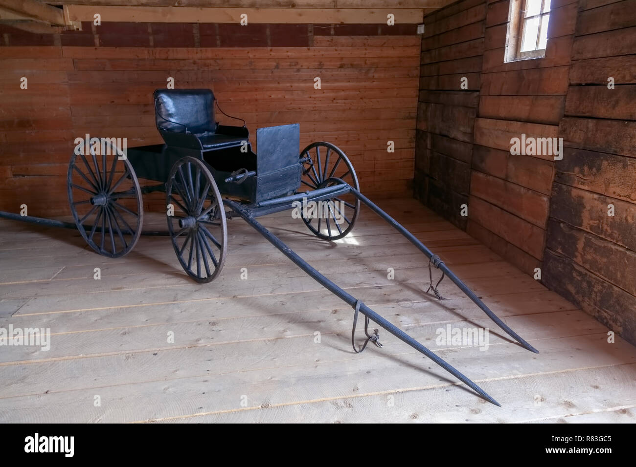 Old black leather seat 2-wheeled antique Horse Drawn Amish Runabout , 'Courting Buggy', Wagon, buggy, carriage inside a farm wooden building Stock Photo