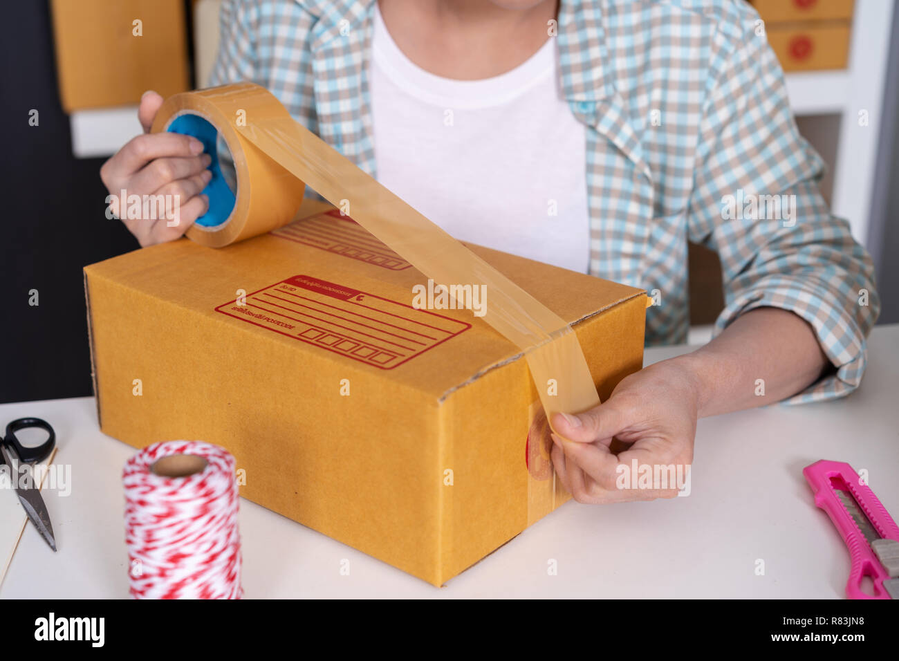 close up hand of woman online entrepreneur using tape to packing parcel box at home office, prepare product for deliver to customer. Stock Photo