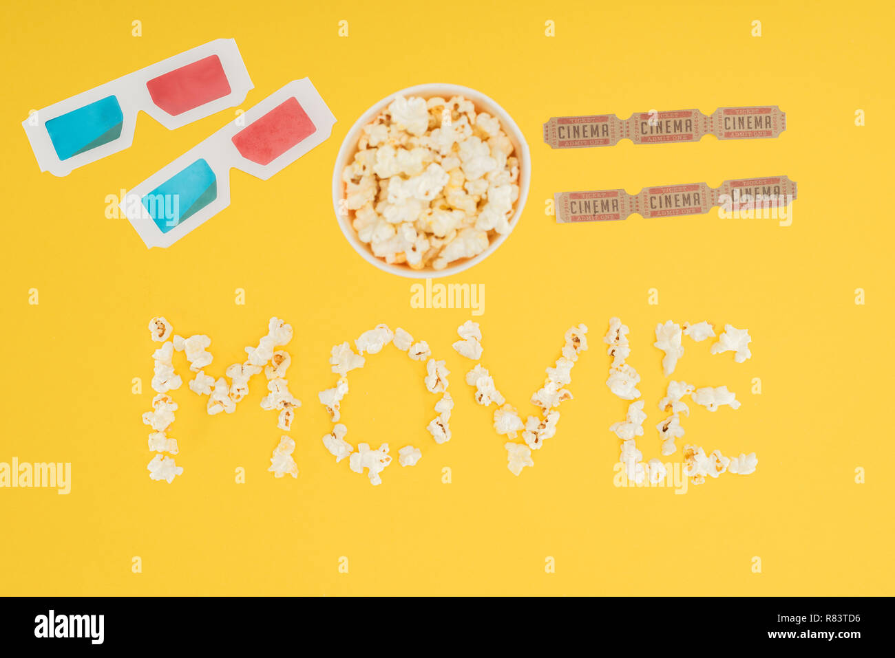 top view of 3d glasses, bucket with popcorn, cinema tickets and 'movie' lettering made with popcorn isolated on yellow Stock Photo