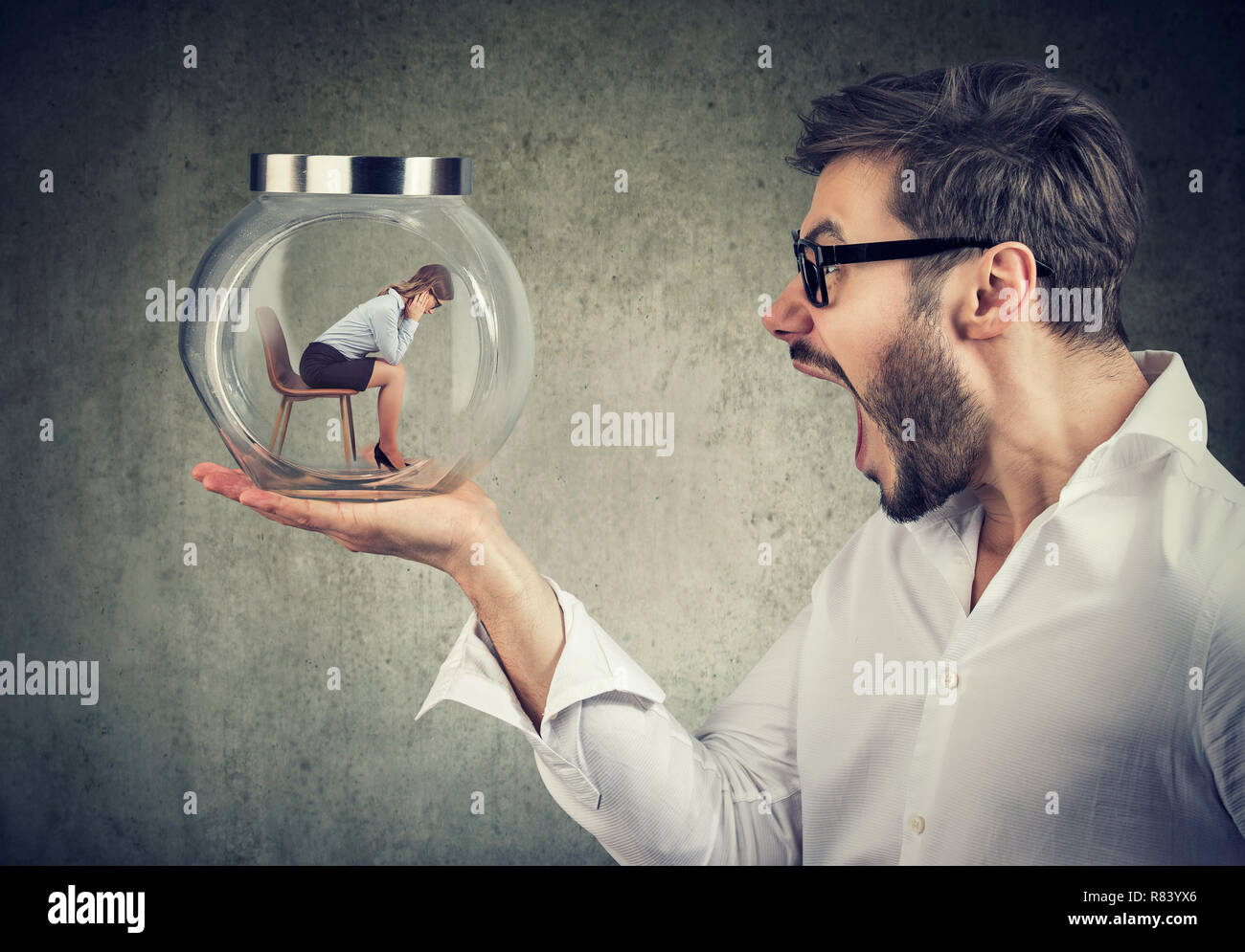 Side view of angry yelling man holding glass jar with captured woman for concept of relationship harassment Stock Photo