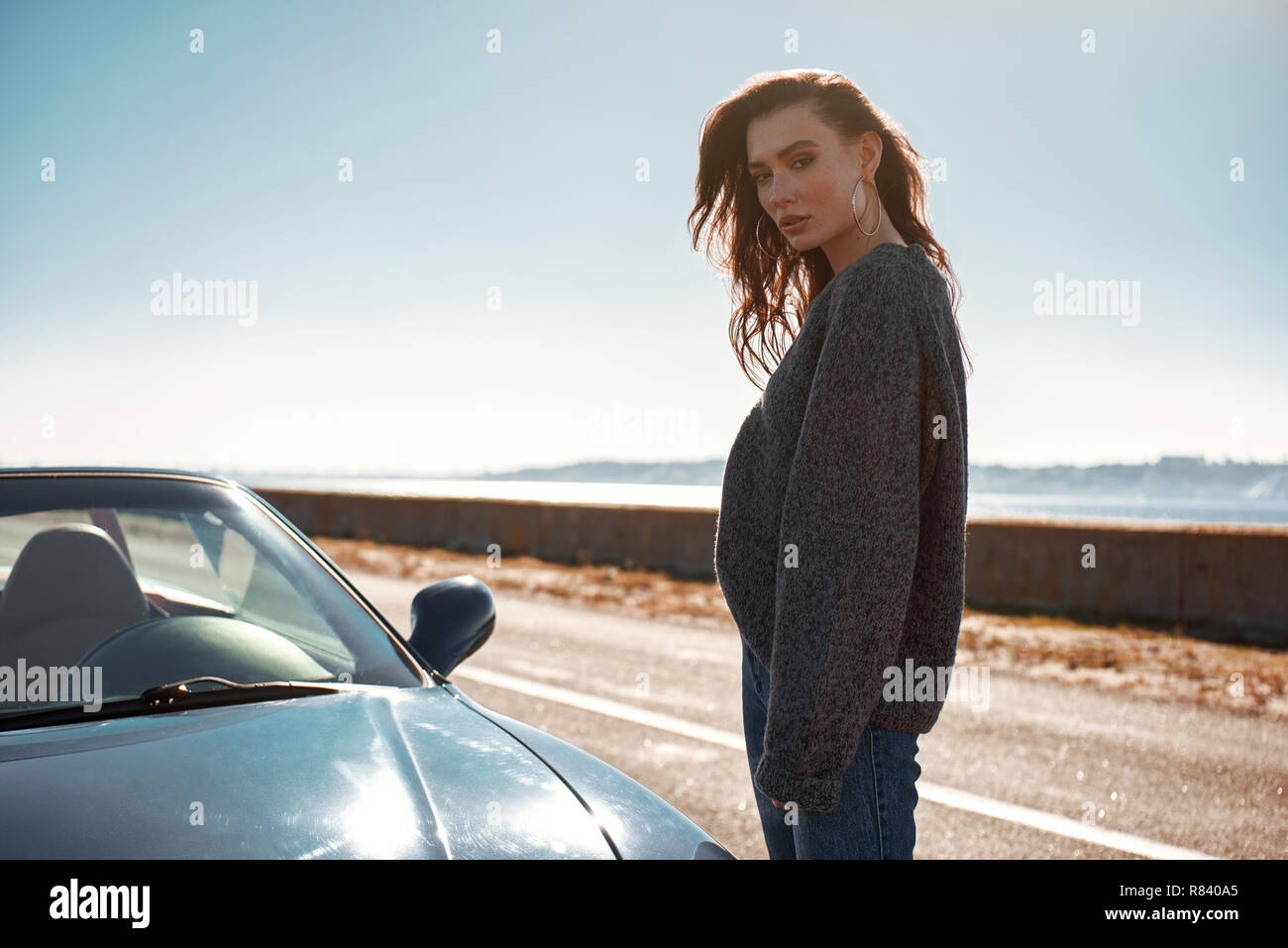 Young woman standing near roofless car outdoors on sunny day near the road Stock Photo