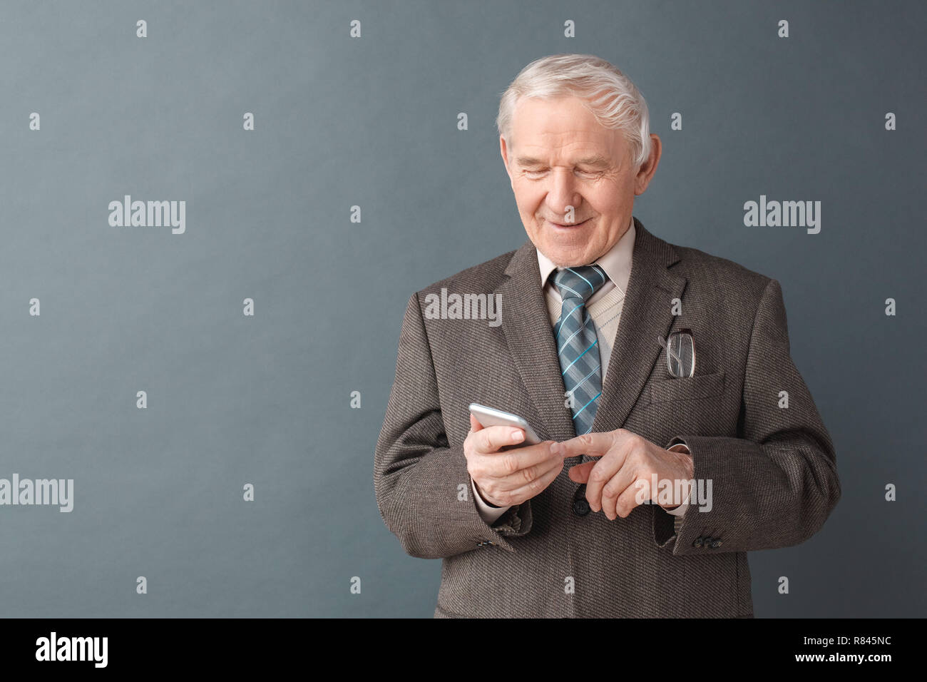 Senior man studio standing isolated on gray typing message on smartphone smiling cheerful Stock Photo