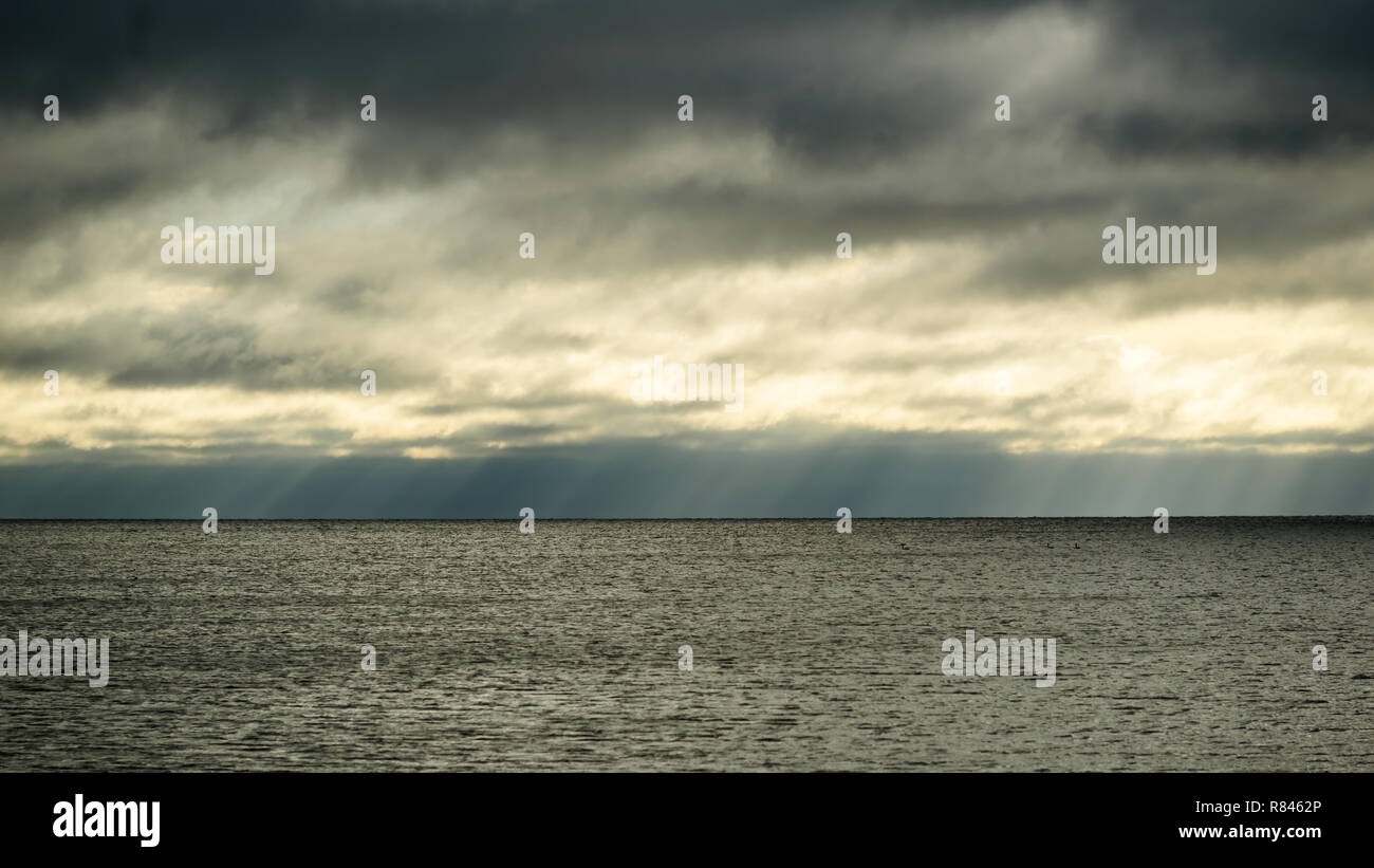 Rainclouds dispersing, letting subtle rays of sunshine through over a dark and sinister horizon. Stock Photo