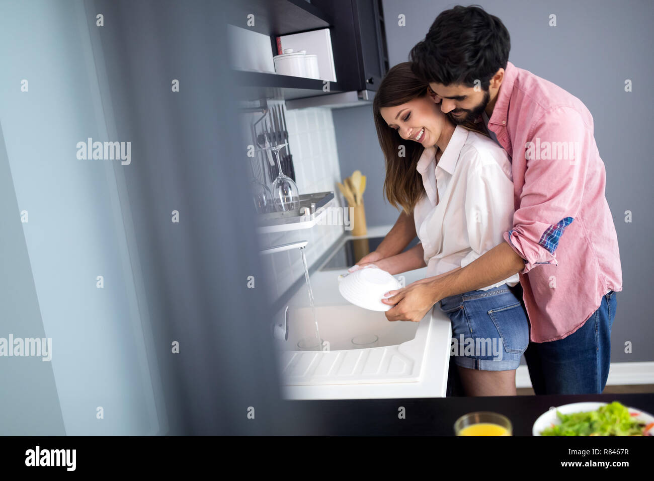 Young happy couple is washing dishes while doing cleaning at home. Stock Photo