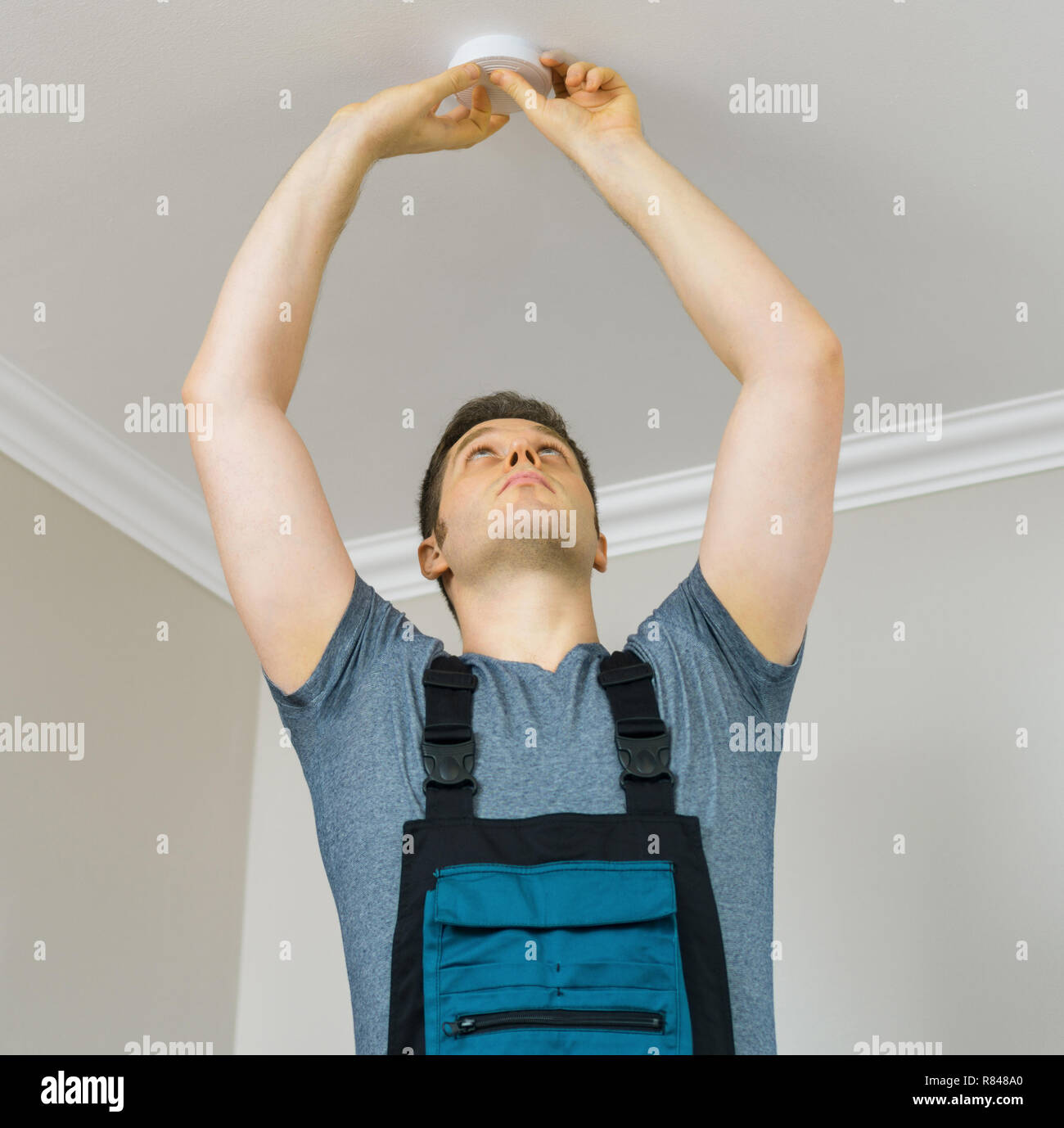 Man mounting smoke detector on the ceiling. Stock Photo
