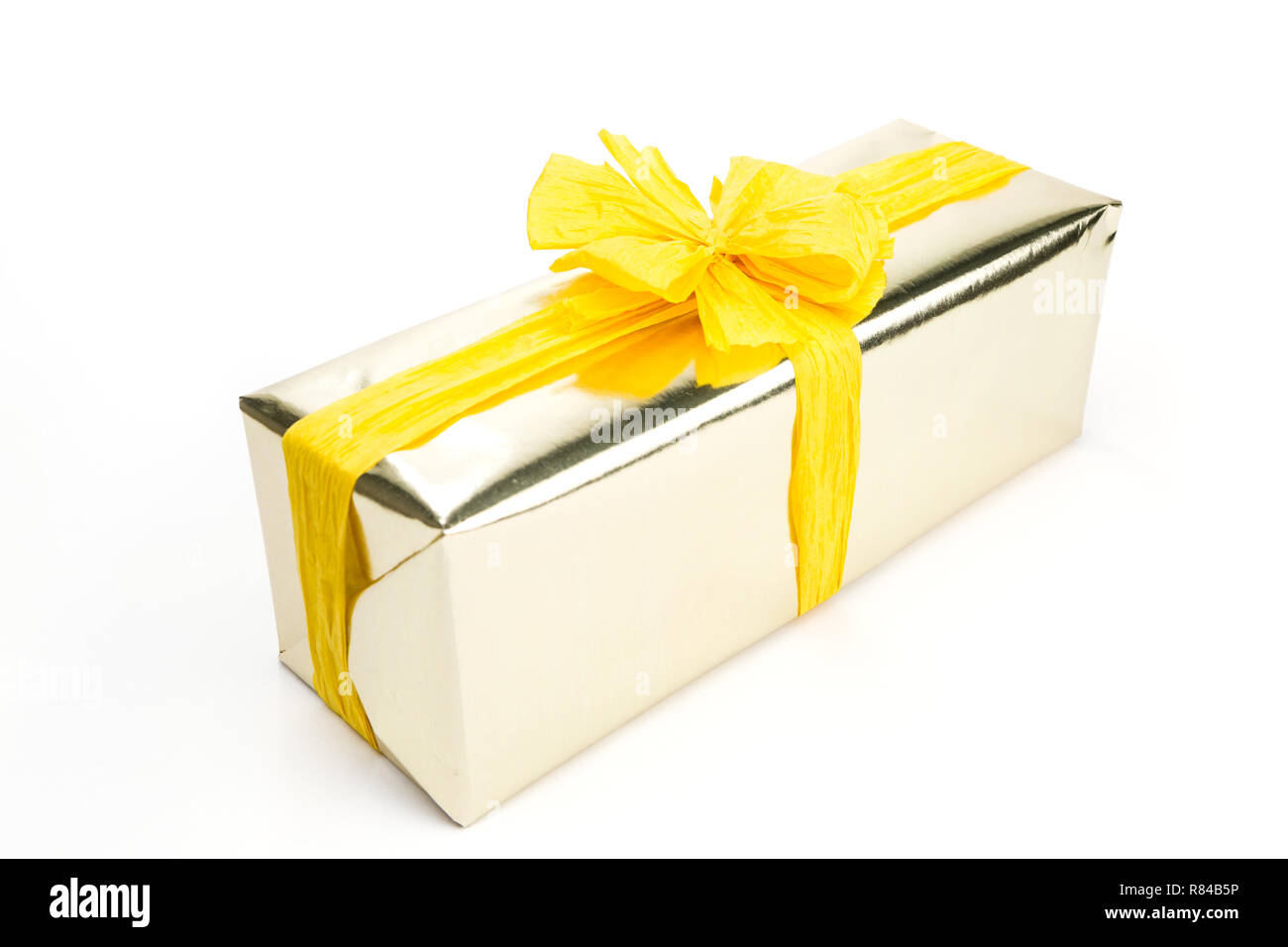 Gift box wrapped in golden wrapping paper, decorated with yellow raffia ribbon and bow on the