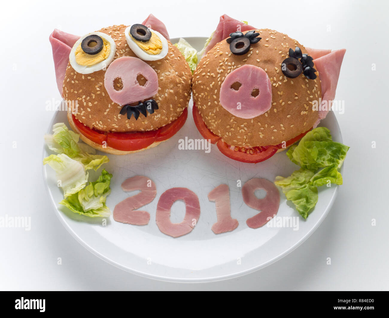 Funny piggies couple burgers, lettuce salad and 2019 digits made of the pork ham as a symbol of new year. Animal chinese horoscope. Stock Photo