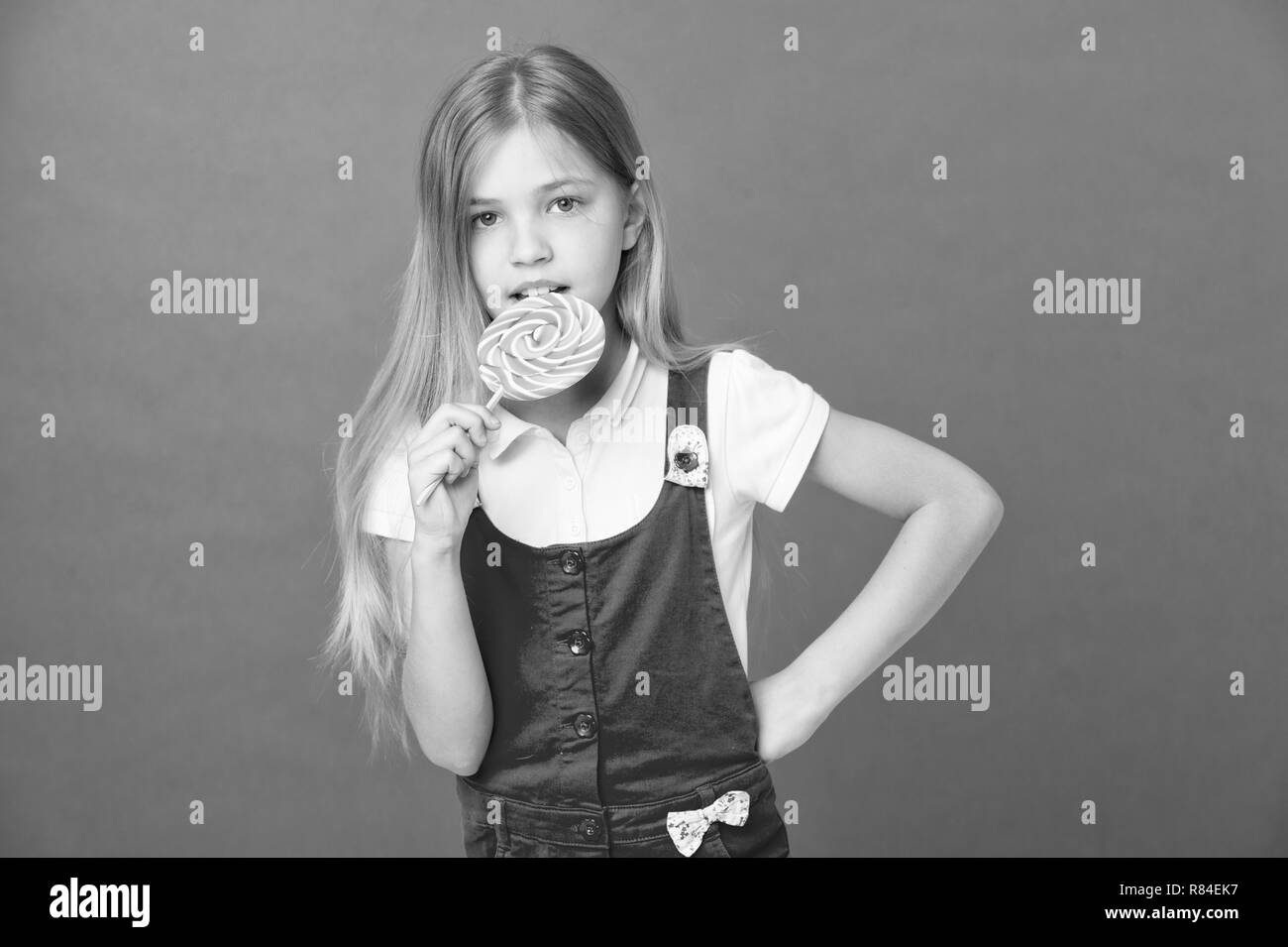 Kid eat lollipop on violet background. Little girl with swirl caramel. Child eating candy on