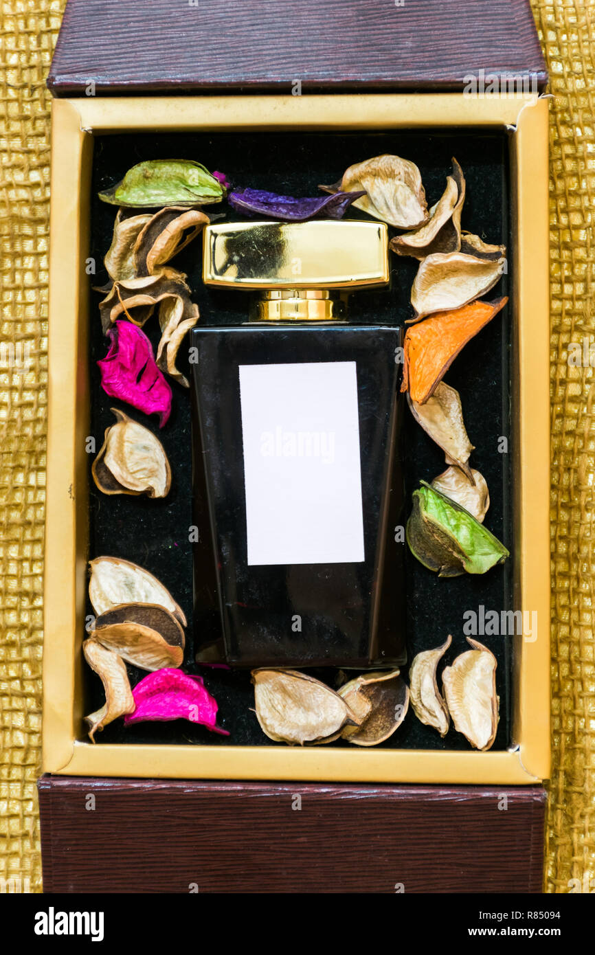 Perfume glass bottle inside golden gift box and colorful leaves with white blank label Stock Photo