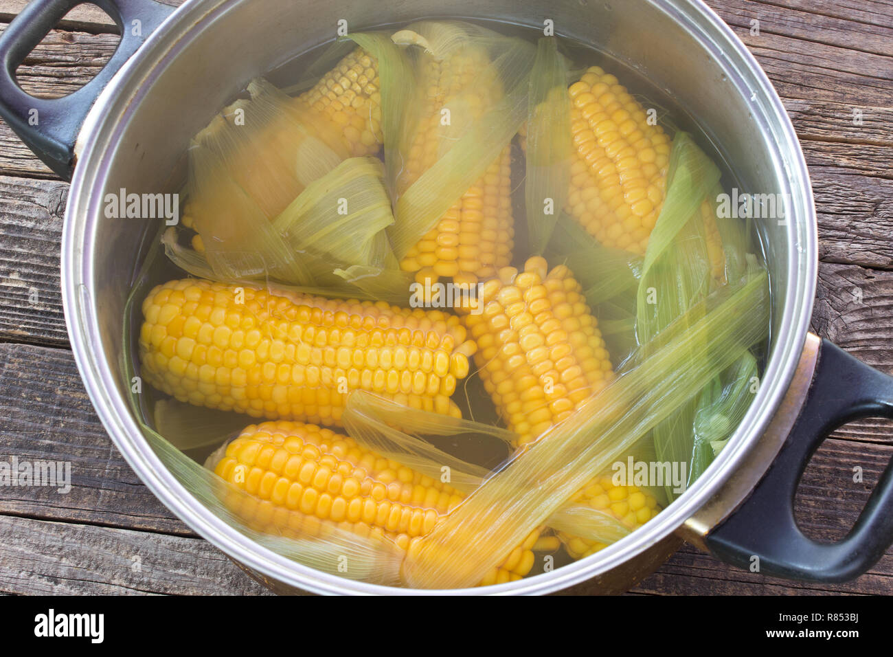 Cooked corn cobs in pot on wooden table Stock Photo