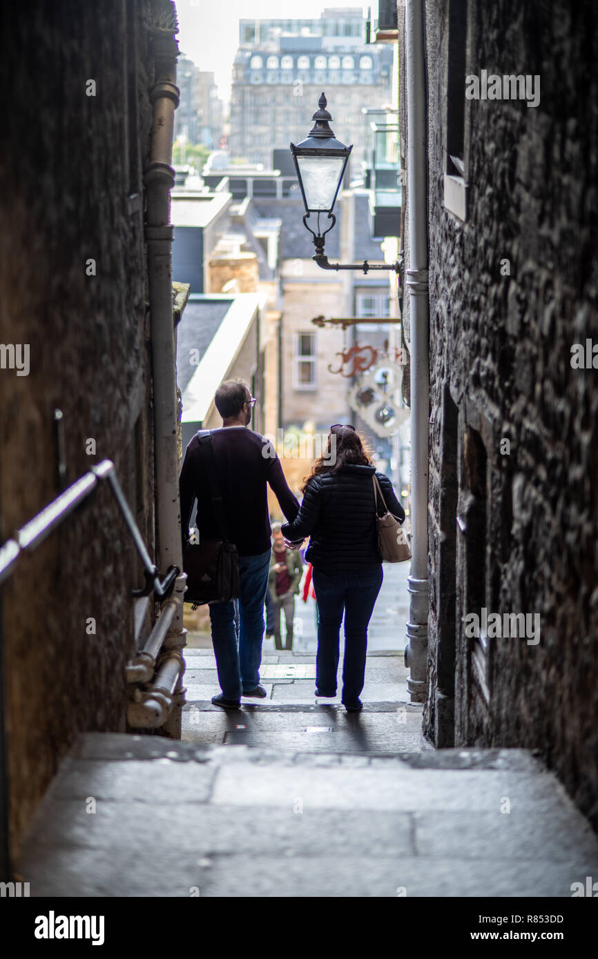 A couple holds hands and walks down stairs in a narrow Edinburgh alley