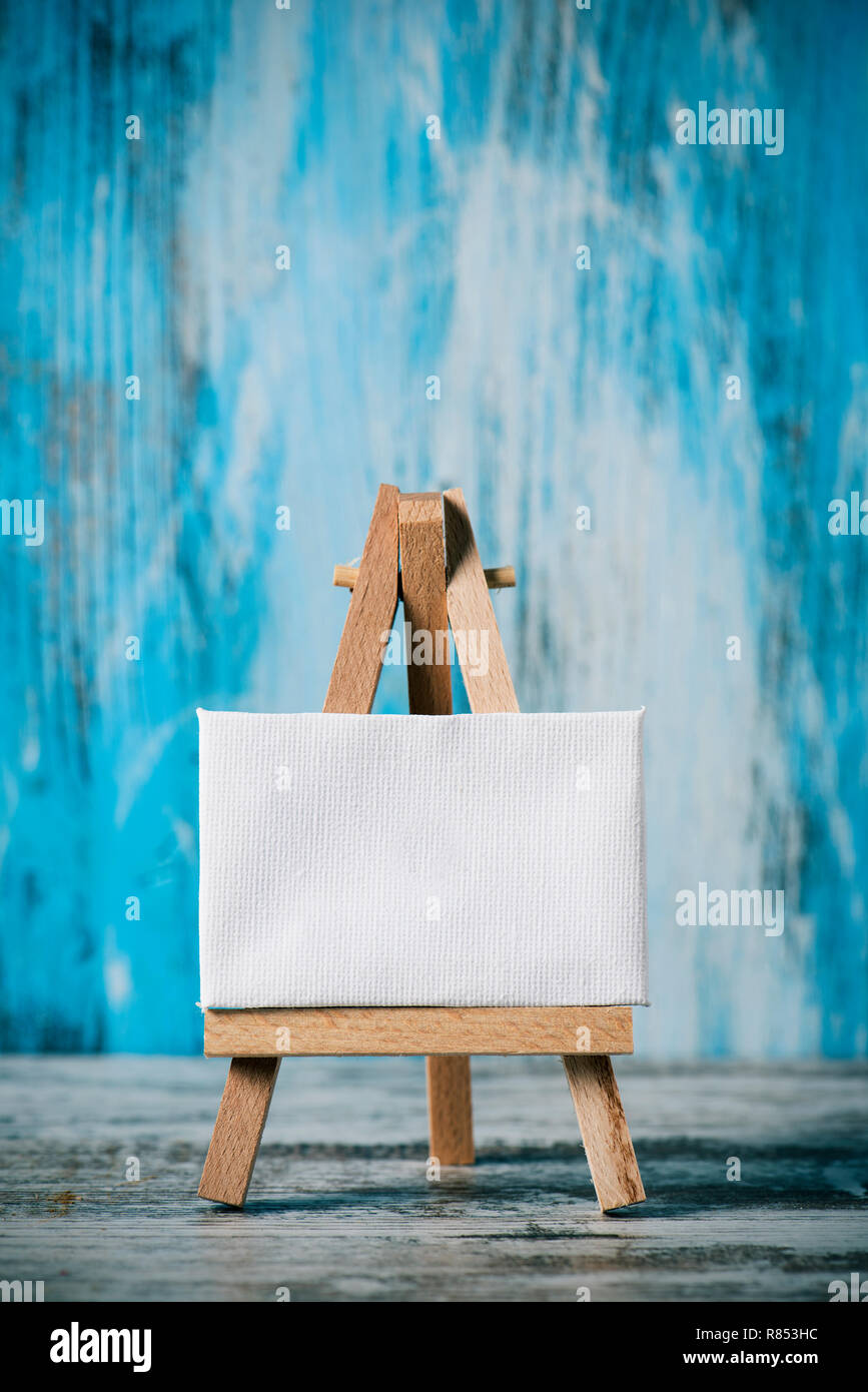 a blank white canvas on a wooden easel, on a wooden surface, against a blue rustic wooden background Stock Photo