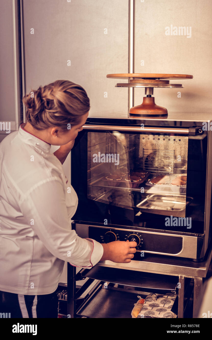 Time to bake. Mice young woman looking at the muffins while setting the