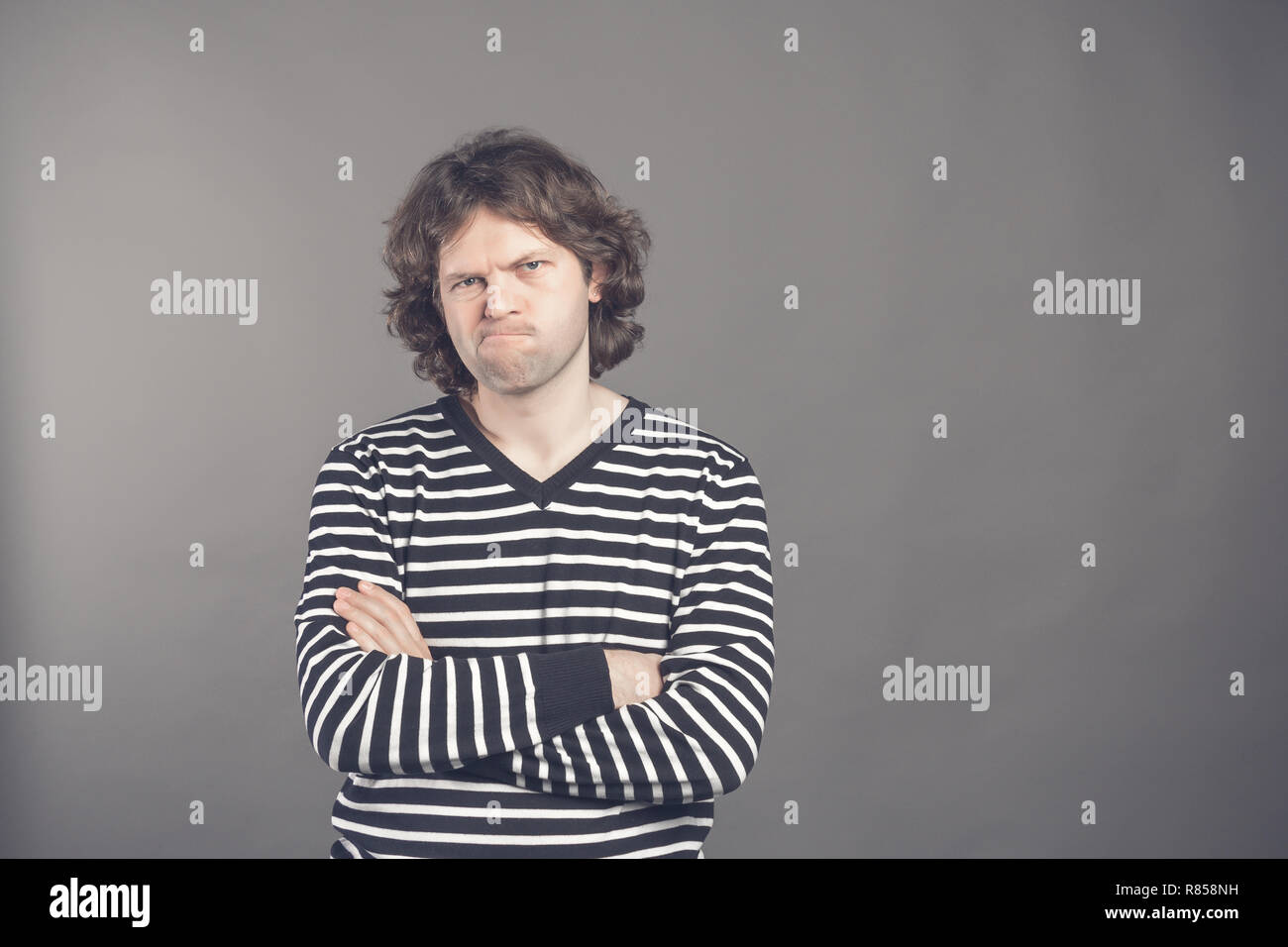 Closeup portrait of displeased, angry, grumpy man in striped sweater bad attitude, arms crossed, folded, looking at you, isolated gray background. Neg Stock Photo