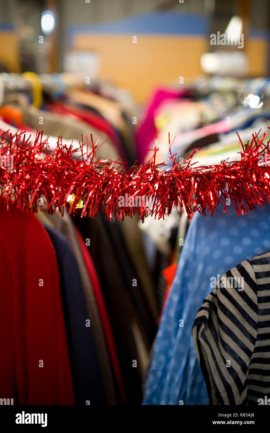 a meagre red metallic tinsel decorates and hangs between two rows of hanging clothes on hangers at a flea market Stock Photo