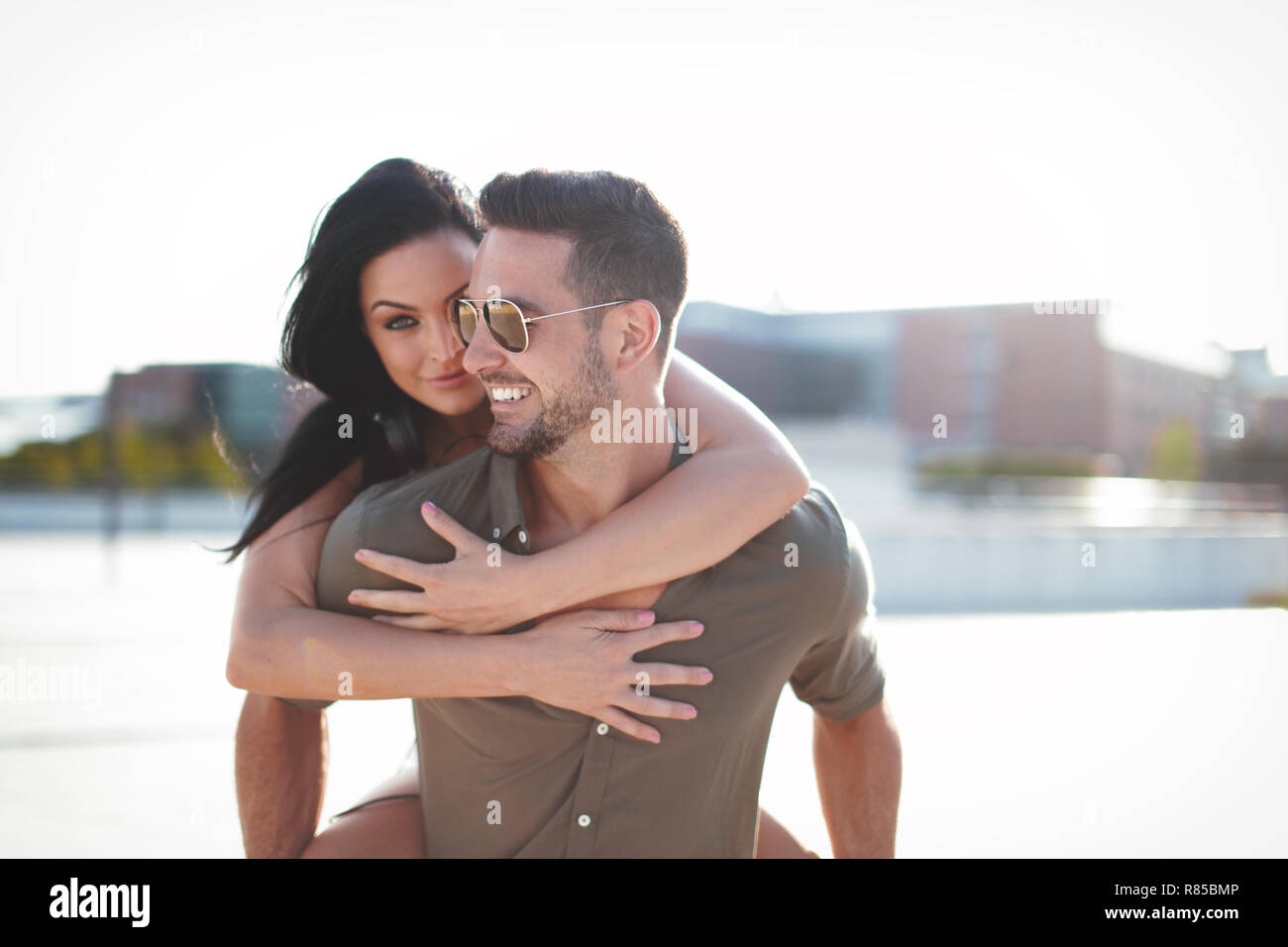 Happy young caucasian urban couple doing piggyback at outdoors, happiness, woman hiding and embracing man Stock Photo