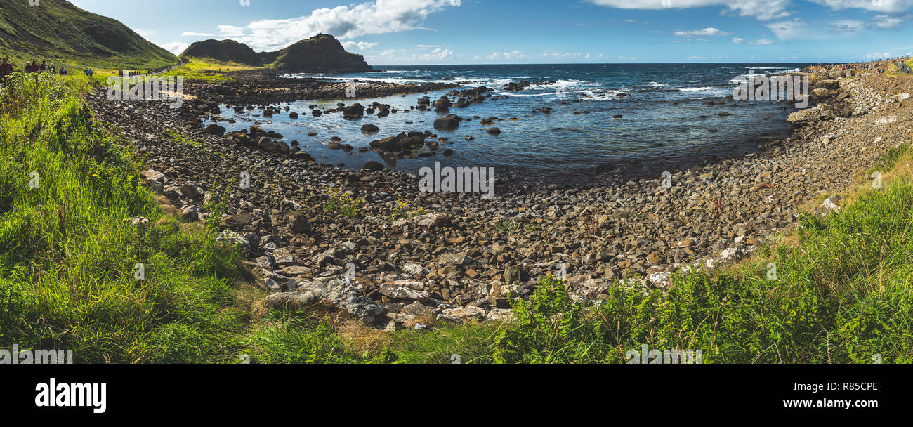 Panoramic view of Northern Ireland bay. Stunning shoreline surrounded by the boulders. Grass covered land under the blue cloudy sky. Wild nature environment. Overwhelming Irish landscape. Stock Photo