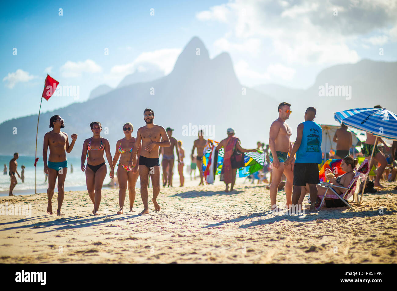 RIO DE JANEIRO - FEBRUARY, 2018: Beachgoers stroll along the shore of Ipanema Beach under a red flag warning for high surf. Stock Photo