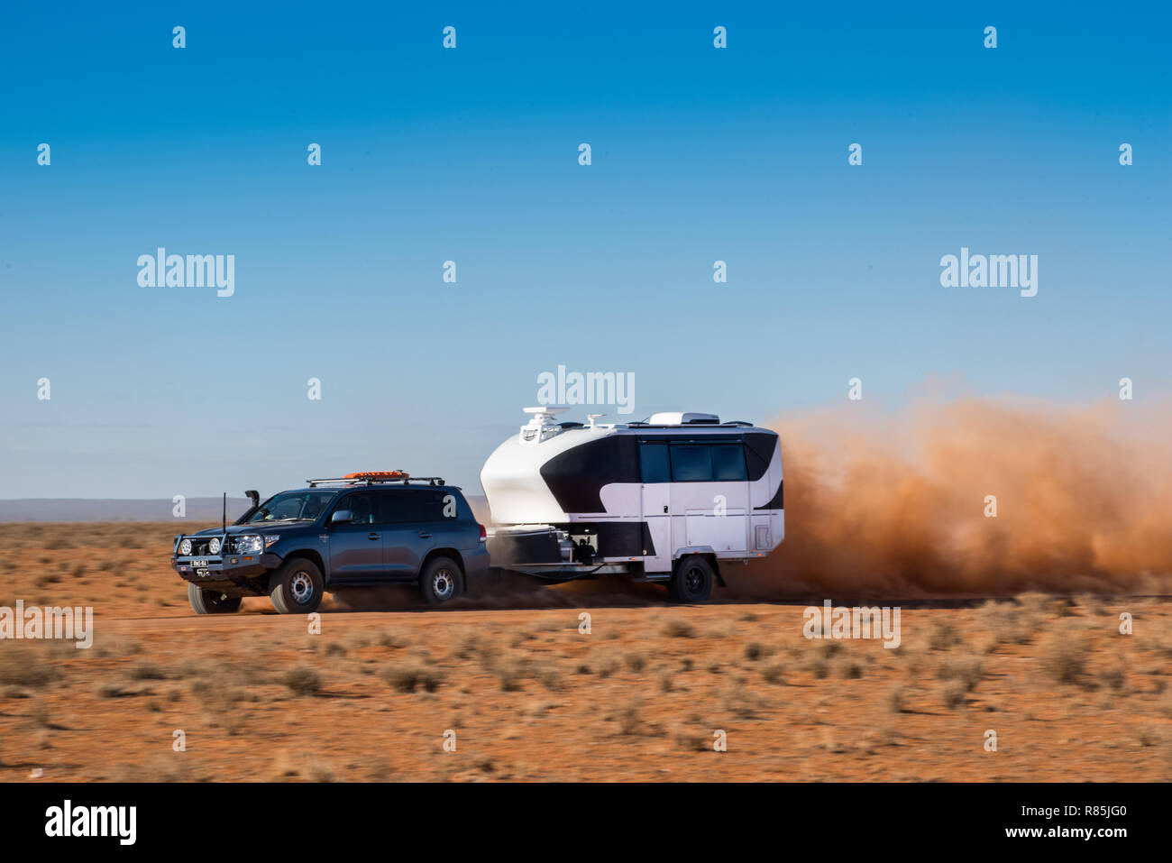 Blue 4wd Toyota LandCruiser towing large, off-road caravan through bull dust on outback Australia red dirt road. Stock Photo