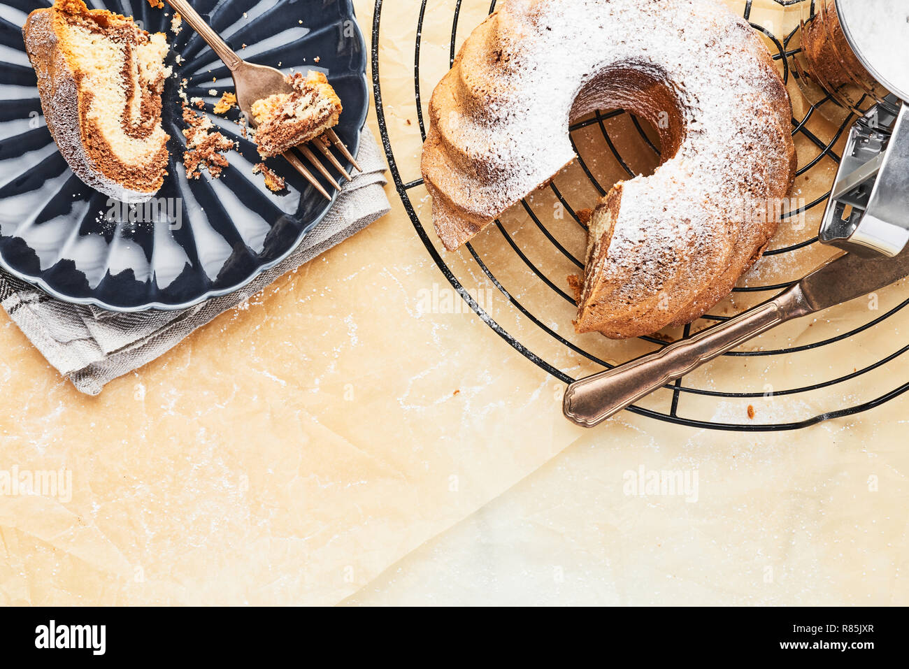 Marble bundt cake on french cooling rack with powdered sugar and one slice of cake on dark blue