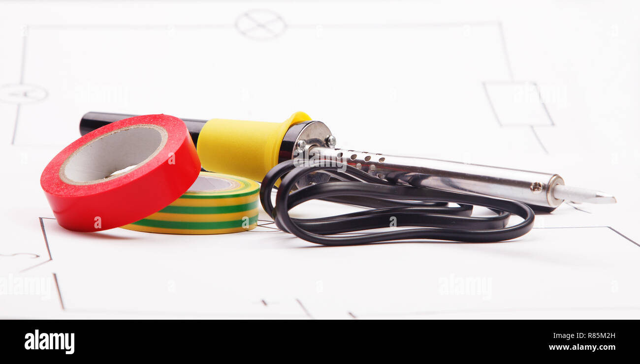 A soldering iron and adhesive plastic tape on the background of the electric scheme Stock Photo