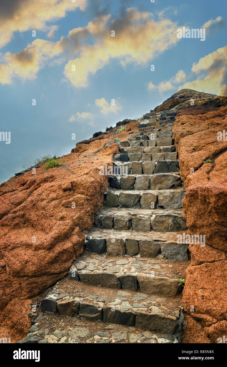 Deserted volcanic rock with natural gray stone stairs to the top of the hill. Blue sky with golden sunset clouds. Landscape with part of popular hikin Stock Photo