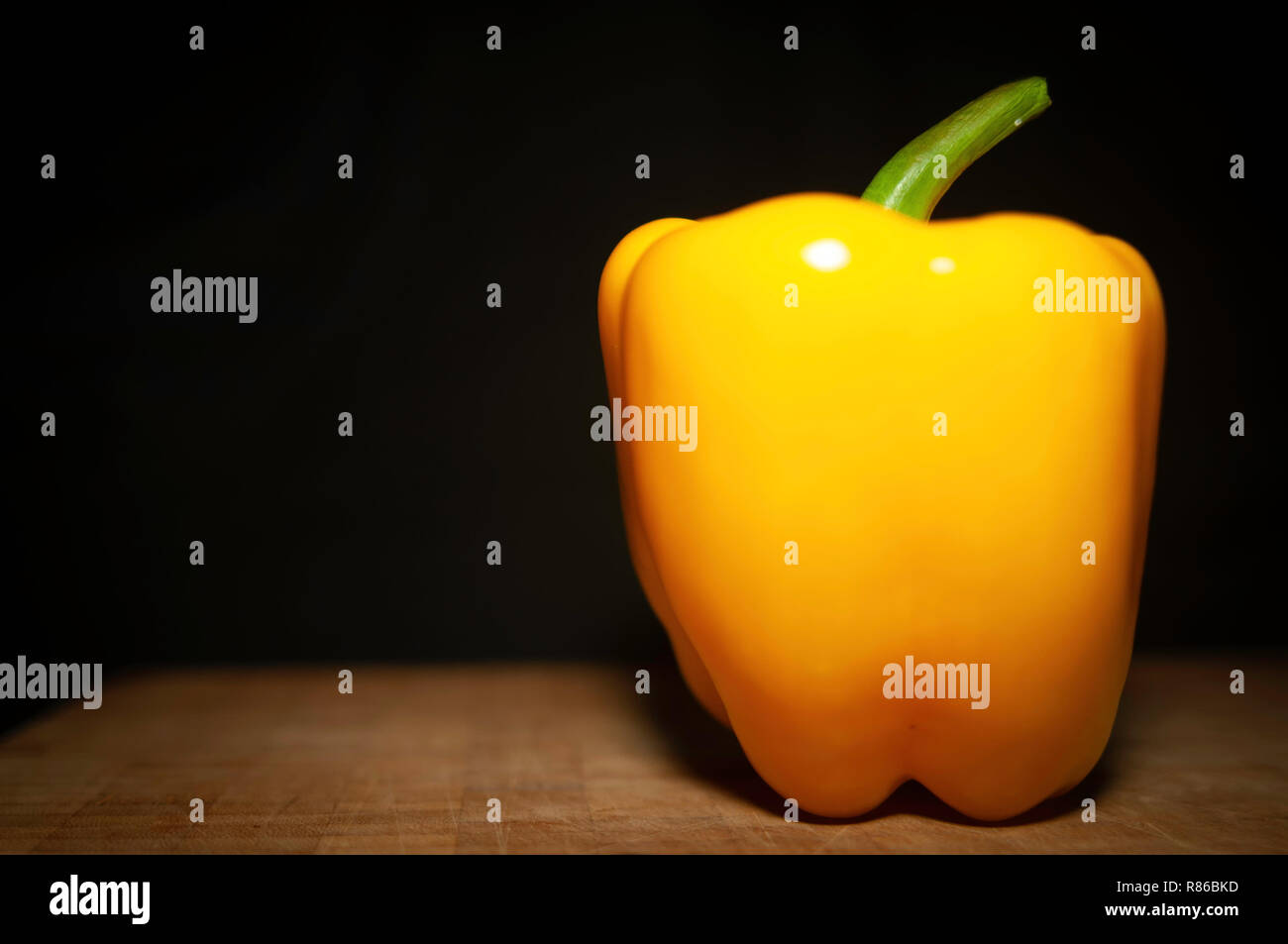Still life of a yellow pepper on a wood cutting board Stock Photo - Alamy