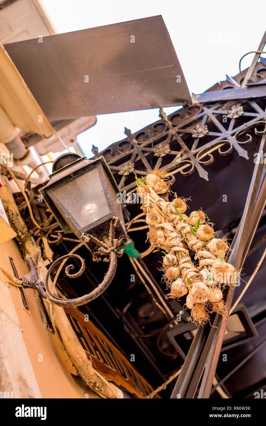 Very old rotten garlic braid hanging out in the street next to vintage street lamp and wrought iron decorations in downtown Corfu, Kerkyra Island Stock Photo