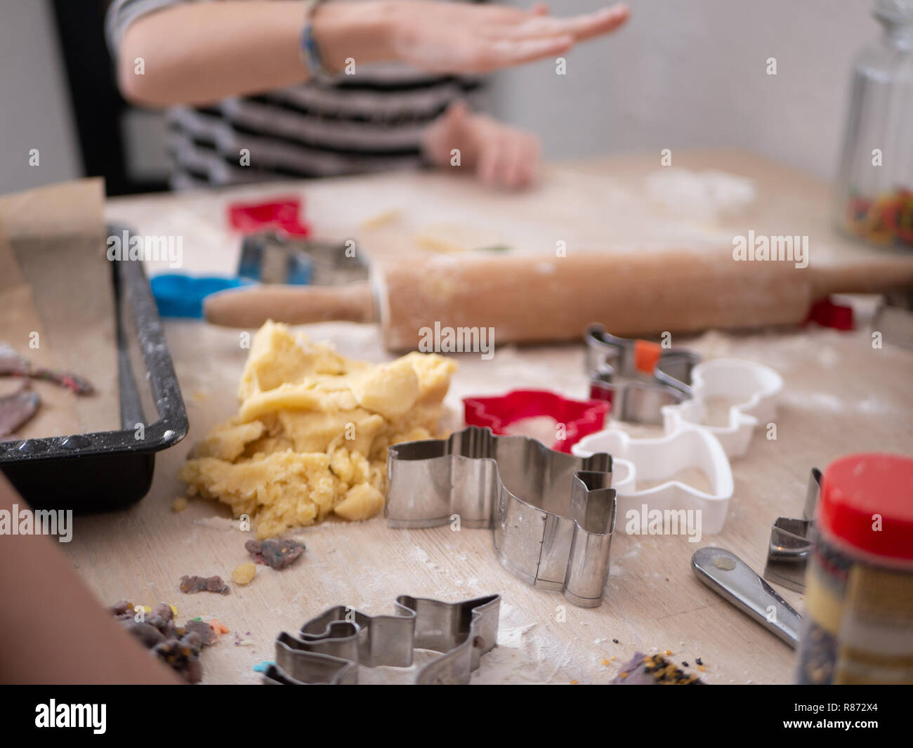 Christmas Chaos: Baking supplies in foreground and little girl forming cookie dough in background Stock Photo